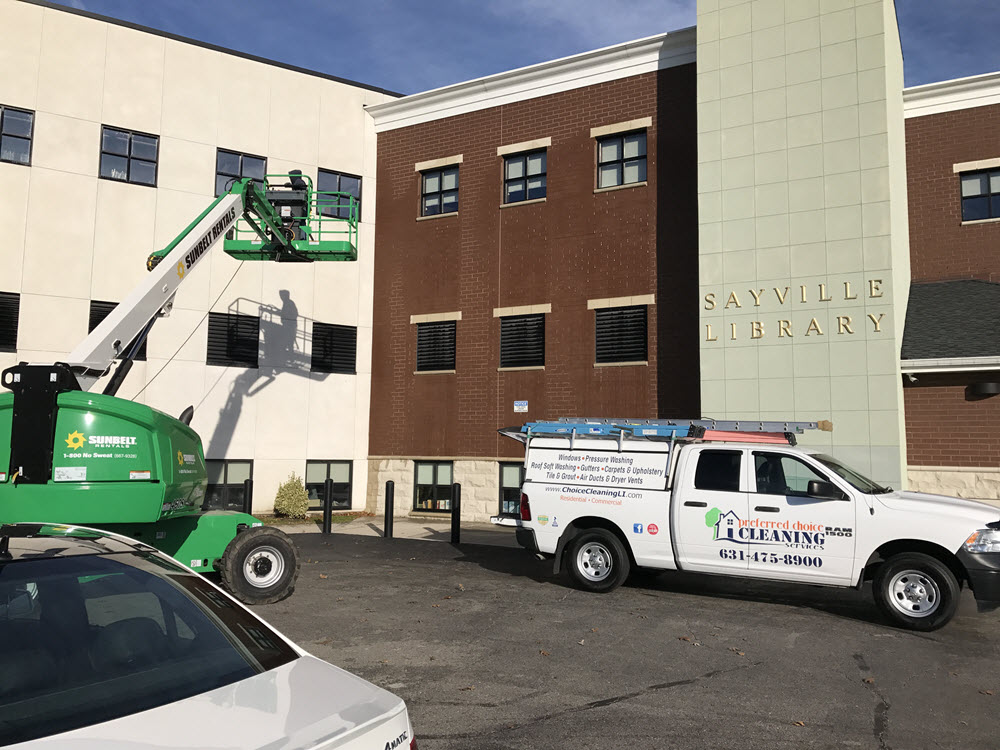 pressure washing professional on lift cleaning side of commercial property building